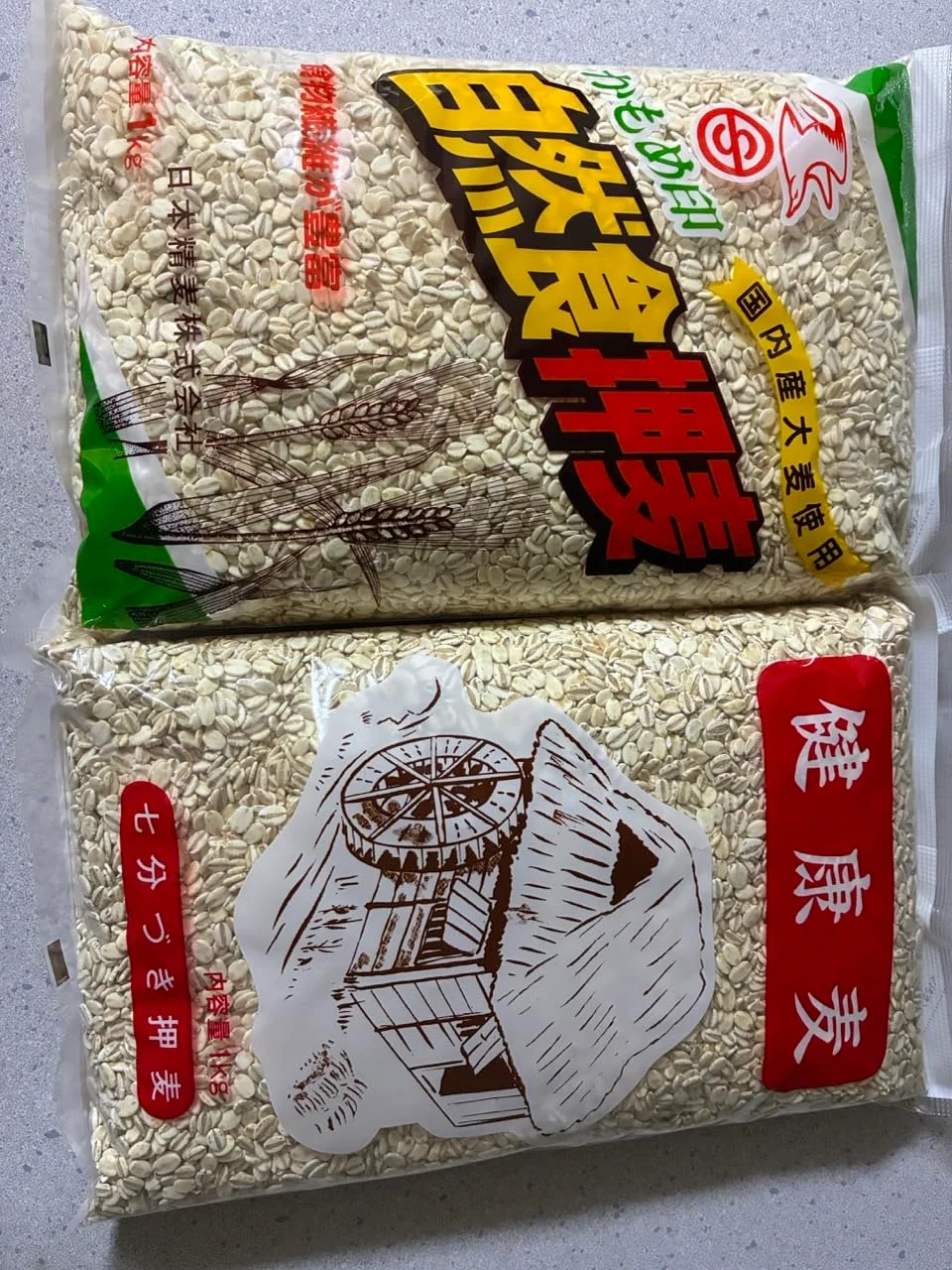 上にかもめ印押麦、下に健康麦の1kg袋を並べた写真。